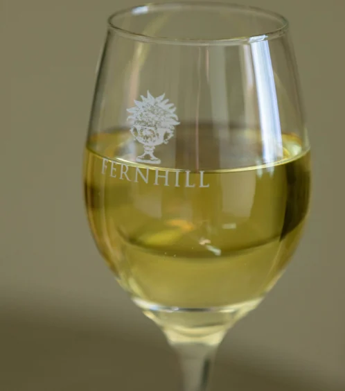 A glass of white wine with "FERNHILL" etched, offering a warm, upscale dining experience.