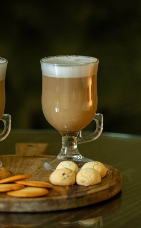 Two mugs of frothy coffee with assorted cookies on a wooden tray in a cosy setting.