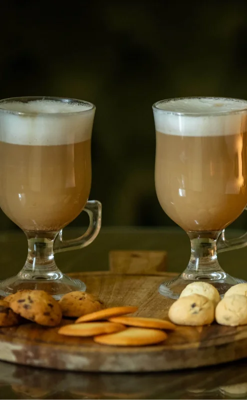 Two creamy coffees and assorted biscuits on a table in a cosy Fernhill House Hotel setting.