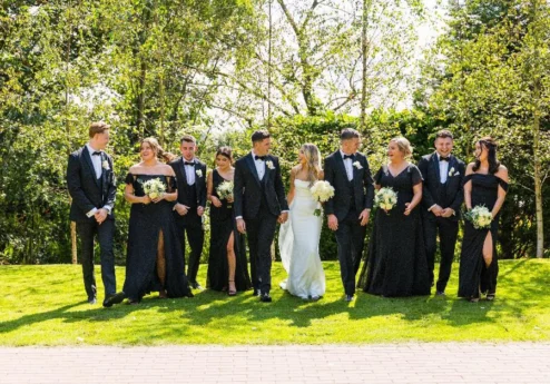 A wedding party in elegant attire poses joyfully on a sunny lawn at Fernhill House Hotel.