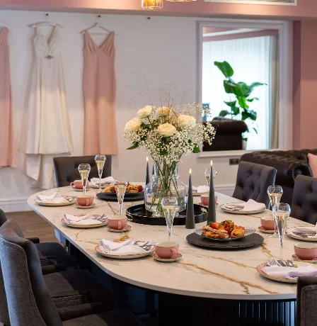 Elegant dining room in hotel with floral centrepiece, dresses hanging, and champagne glasses.