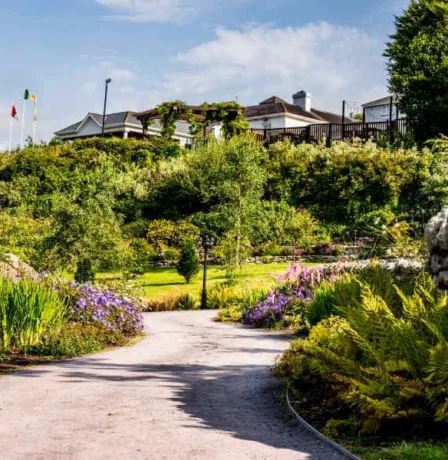 A family strolls through lush gardens towards Fernhill House Hotel on a sunny day.