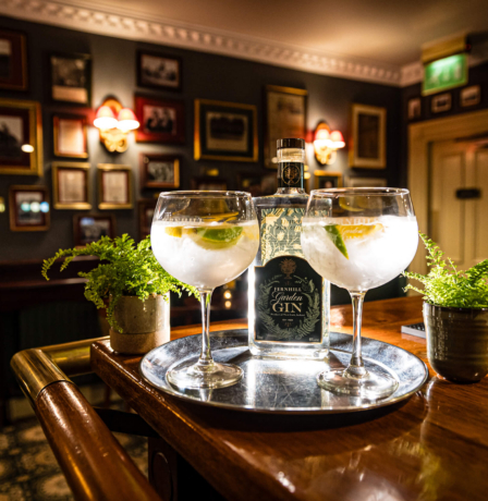 Cosy hotel bar with gin glasses on a wooden counter, surrounded by framed pictures.