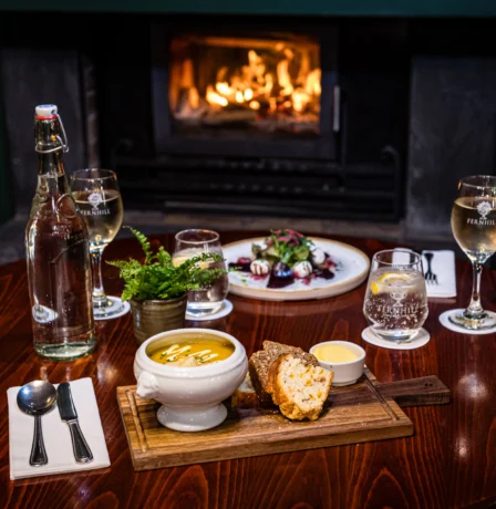 Inviting dining setup with soup and drinks by a cosy fireplace at Fernhill House Hotel.