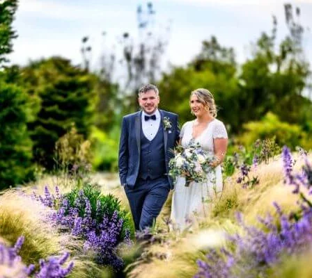 A couple walking through vibrant gardens at Fernhill House Hotel on a sunny day.