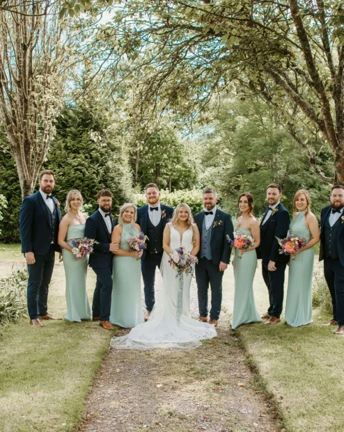 A wedding party poses outdoors at Fernhill House Hotel, surrounded by lush greenery.