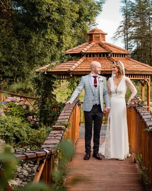 Couple holding hands on a wooden bridge at Fernhill House Hotel garden.