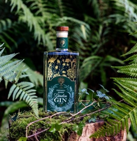 Fernhill House Garden Gin on a mossy tree stump surrounded by lush ferns.
