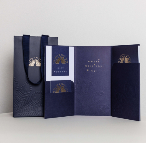 Navy gift voucher and bag on a white surface, embossed with a peacock design.