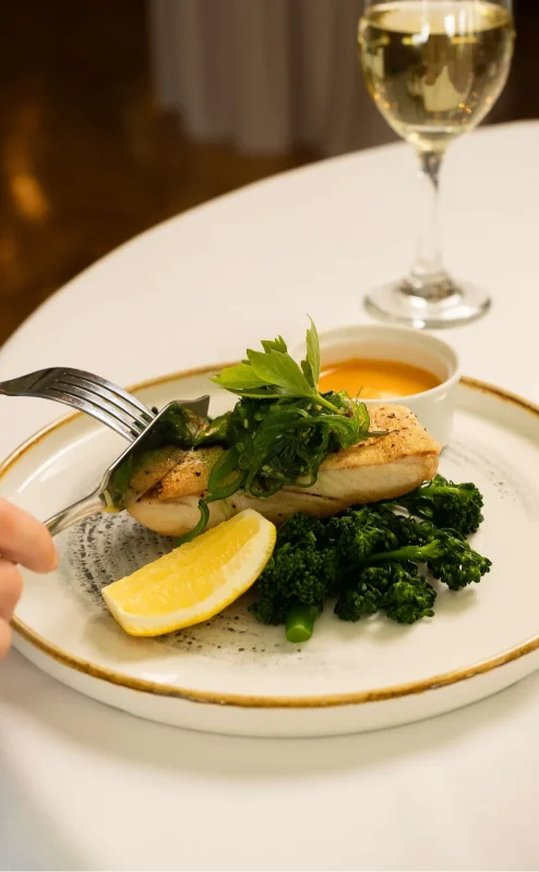 Dining at Fernhill House Hotel, close-up of a dish with fish, greens, and a lemon wedge.