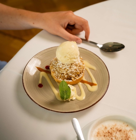 A delicious dessert with ice cream at Fernhill House Hotel, alongside a hand holding a spoon.