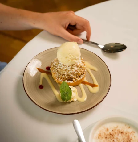 A hand reaches for a dessert with ice cream at Fernhill House Hotel's dining area.