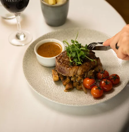 A dining table setting with a steak, roasted tomatoes, and wine at Fernhill House Hotel.