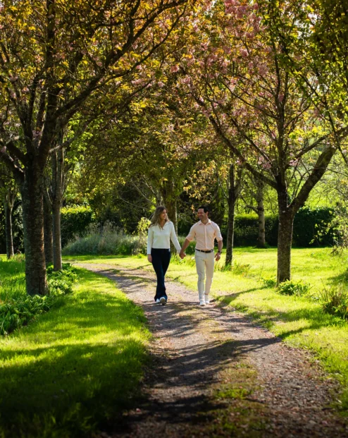 A couple strolls hand-in-hand through sunlit gardens at Fernhill House Hotel.