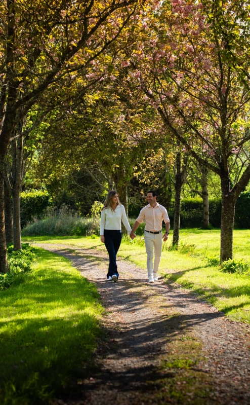 Couple strolling along sunlit path amidst vibrant gardens at Fernhill House Hotel.