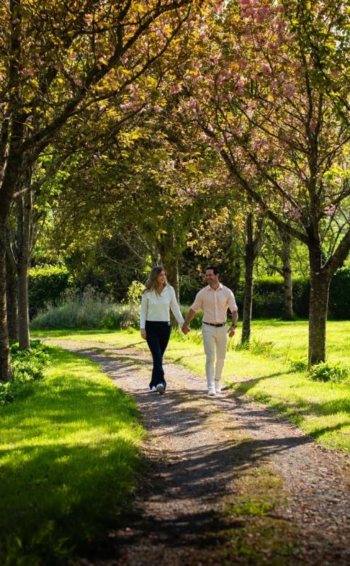 A couple strolls hand-in-hand through sunlit gardens at Fernhill House Hotel.