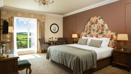 Elegant hotel room with a cosy bed, seating area, and countryside view.