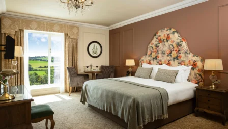 Elegant hotel room with countryside view, featuring a plush bed and cosy seating area.