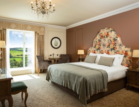 Elegant hotel room with a cosy bed, seating area, and countryside view.