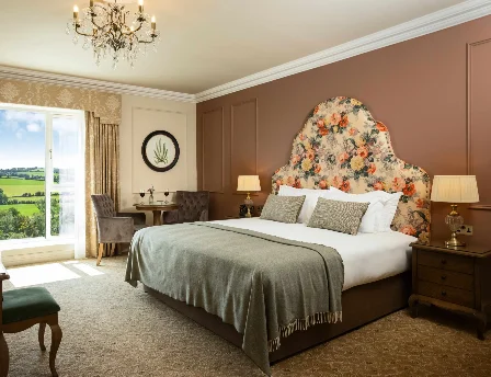 Elegant hotel room with countryside view, featuring a plush bed and cosy seating area.