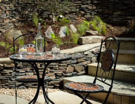 Cosy outdoor patio with drinks at Fernhill House Hotel. Rustic stone walls and plants surround.