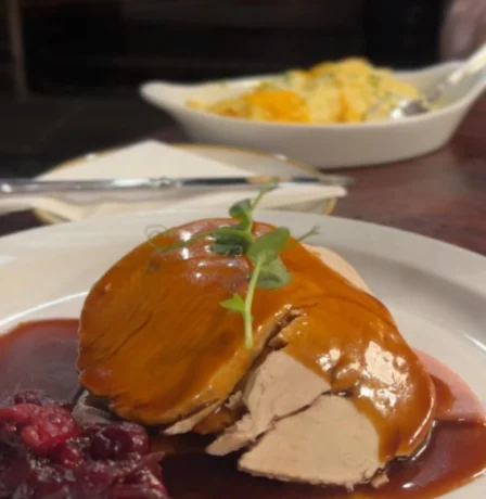 Cosy dining setting with roast turkey and cranberry sauce near a warm fireplace.