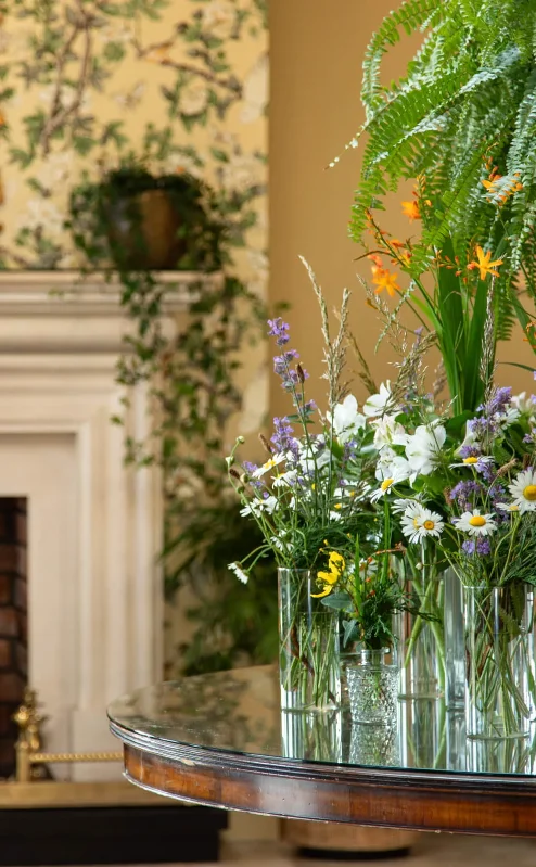 Elegant hotel lobby with a cosy fireplace, floral arrangements, and lush greenery.