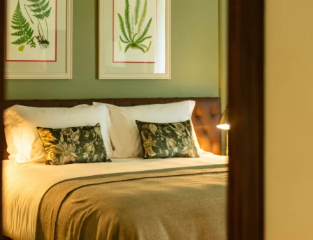 Cosy hotel room with a plush bed, fern artwork, and warm lighting.
