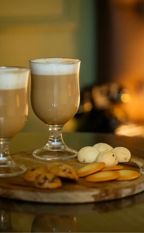 Cosy hotel room with warm lighting, featuring two cappuccinos and a plate of biscuits.
