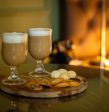 Cosy hotel room with two lattes and biscuits on a table, warm lighting in the background.