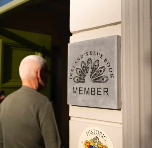 Mature couple entering Fernhill House with member plaque visible on cream wall, warm welcoming scene