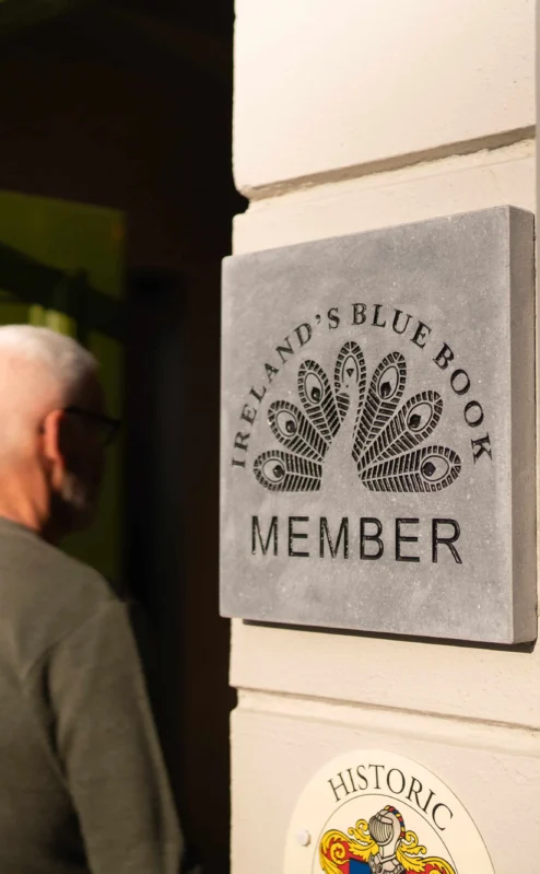 Mature couple entering Fernhill House with member plaque visible on cream wall, warm welcoming scene