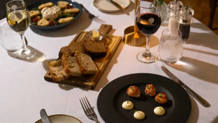 Cosy dinner setup with appetisers, wine, and bread at a warmly lit restaurant table.
