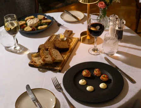 Cosy dinner setup with appetisers, wine, and bread at a warmly lit restaurant table.