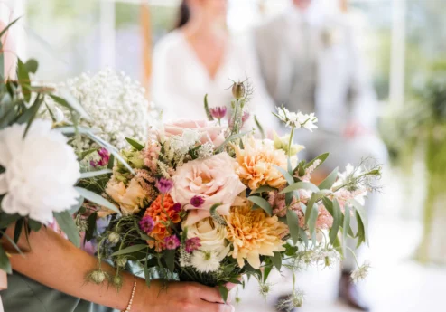 Bride and family holding a pastel bouquet of roses, dahlias and greenery at a relaxed wedding celebration (transcription: Allora CMS)